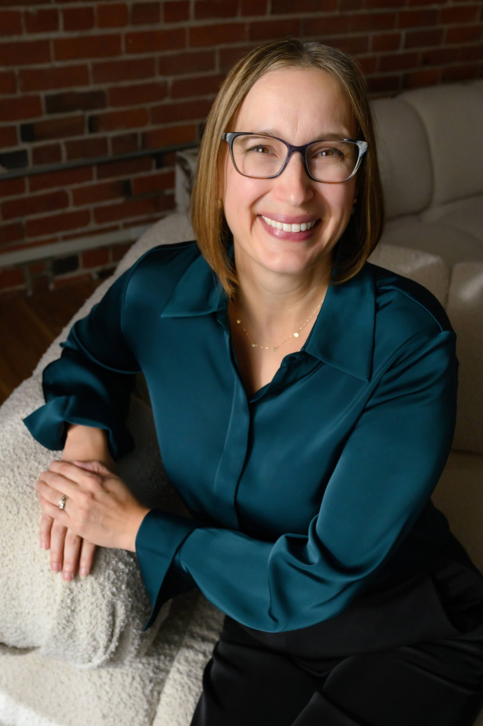Shelley Tice sitting on a couch with a brick wall behind her.